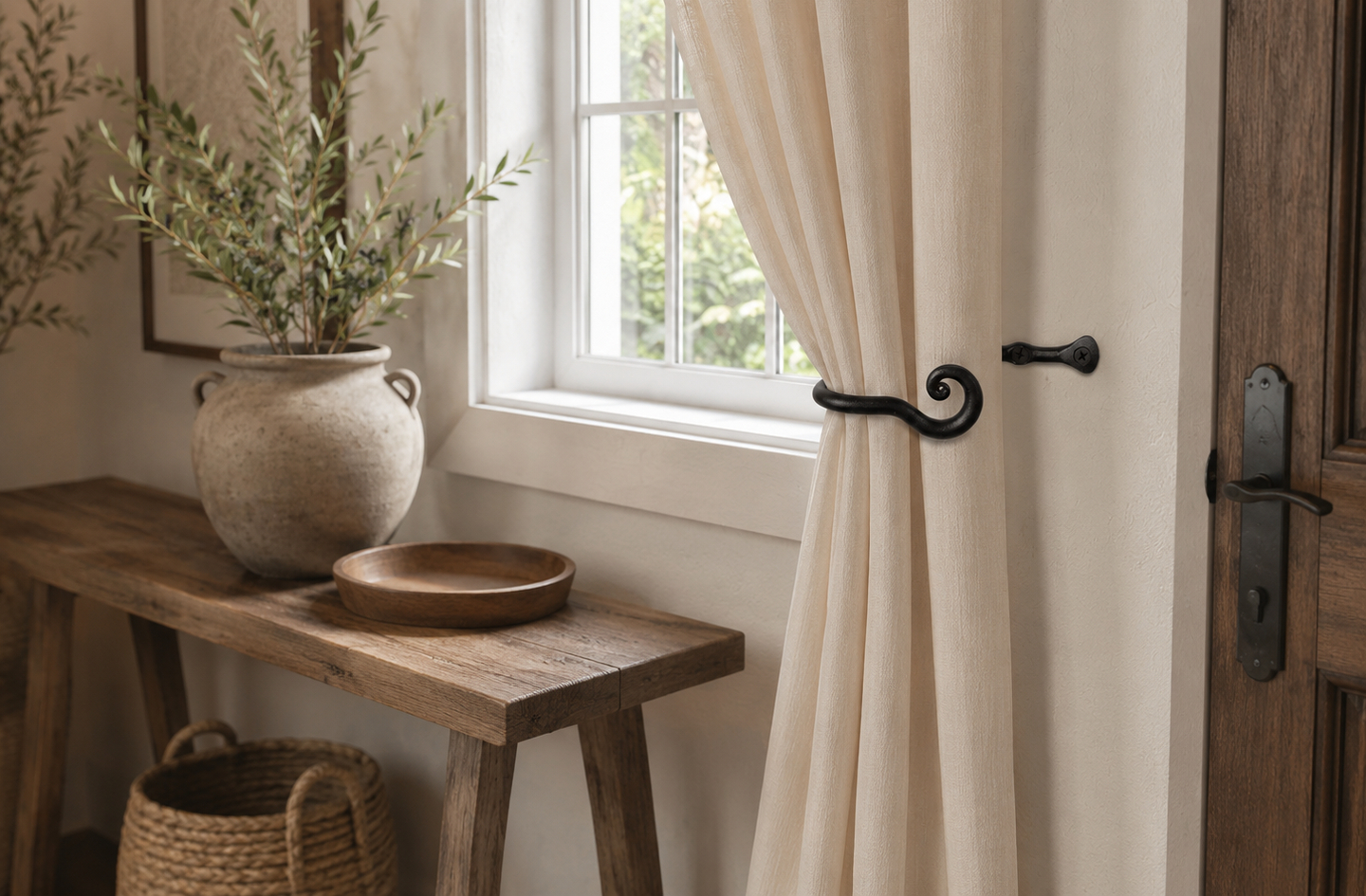 Black wrought iron curtain holdbacks metal mounted beside a window in a rustic farmhouse entryway with wooden console table and ceramic vase
