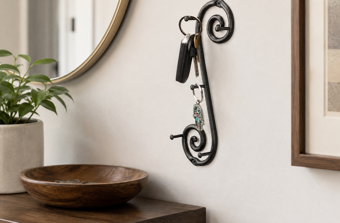 Compact key holder in black wrought iron mounted on a white wall above a console table, with keys hanging from the hooks