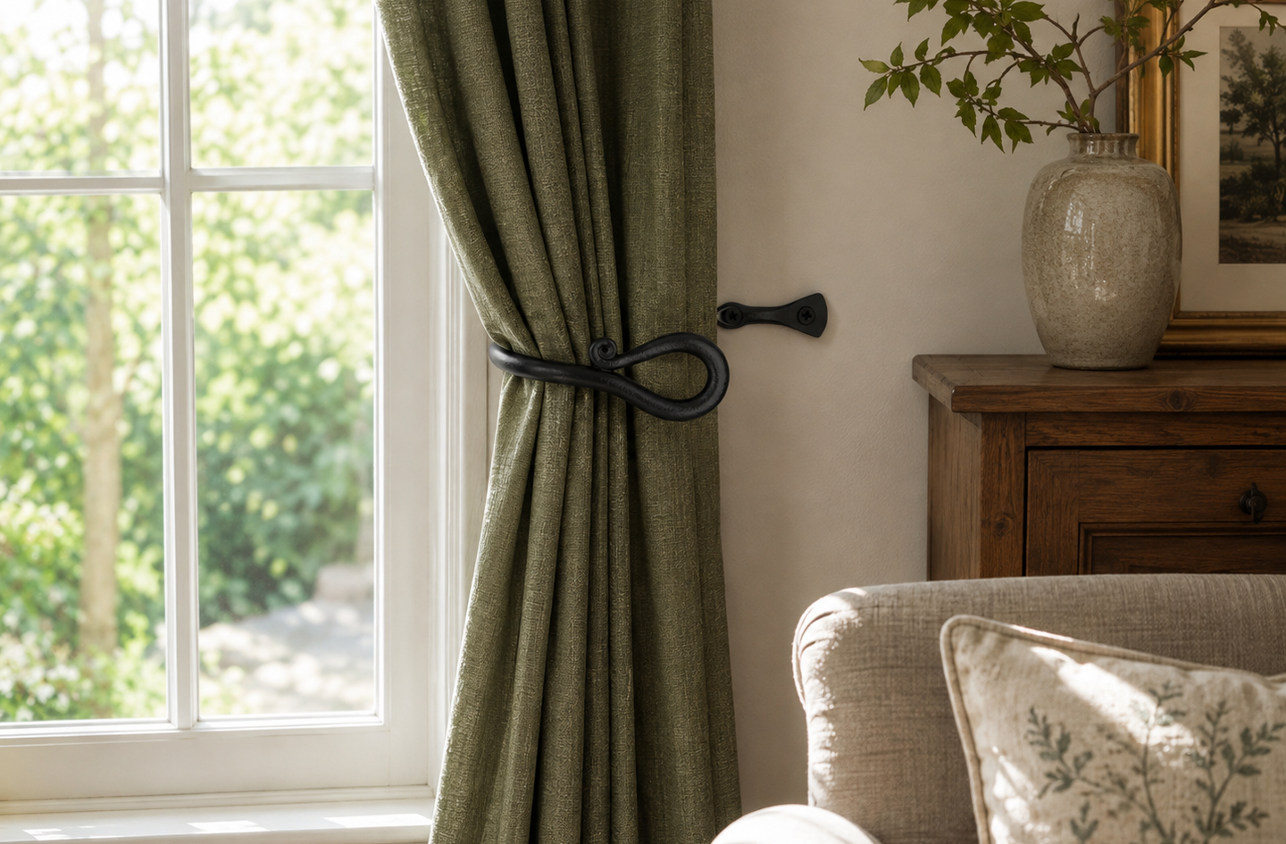 A decorative black metal curtain holdback mounted beside a window, showing proper horizontal clearance from the frame with a green curtain draped naturally to one side