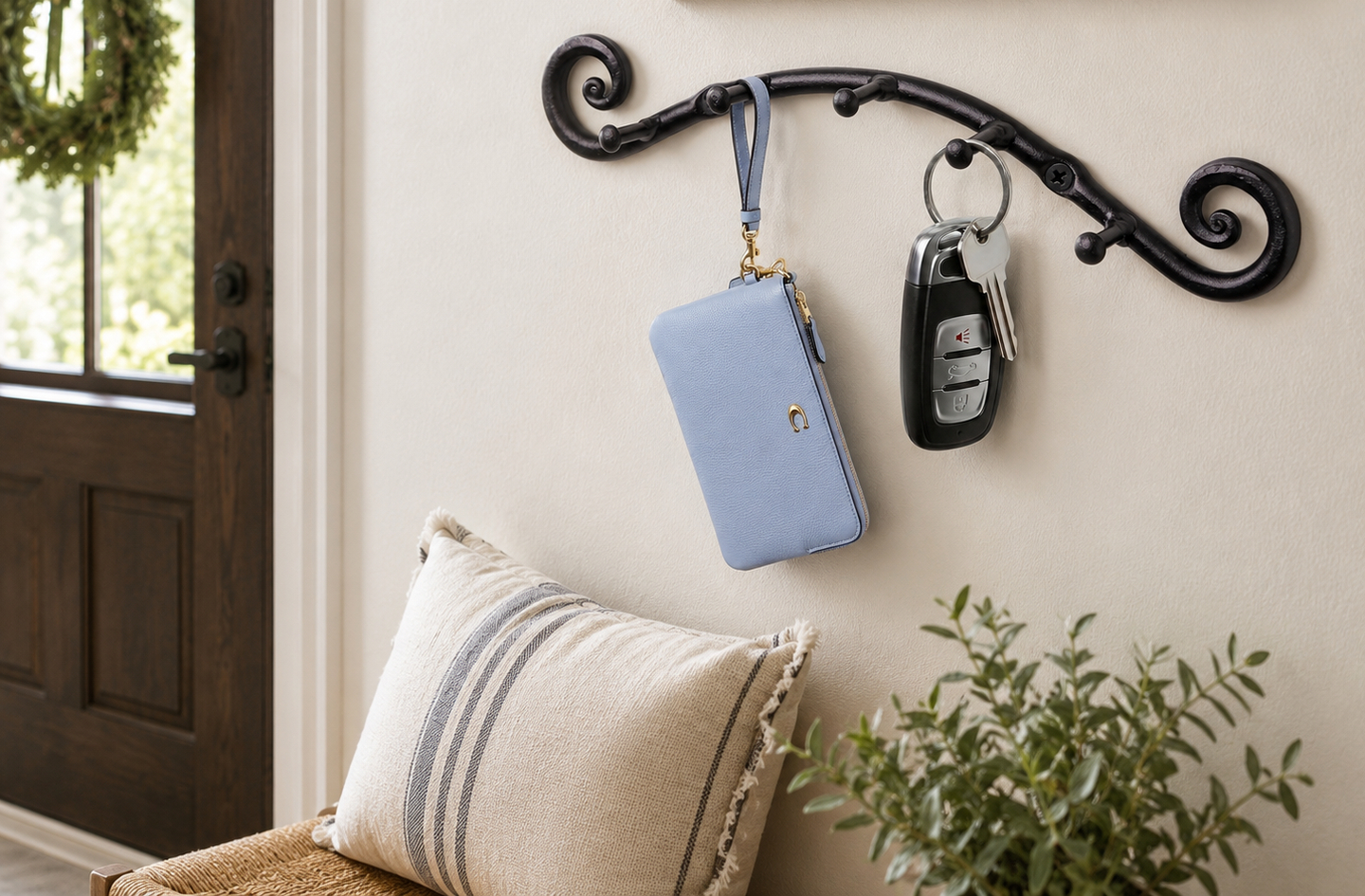 Black swirly wrought iron key holder by a wooden door, holding a car fob and wristlet