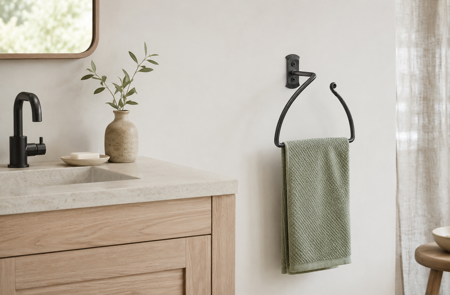 Black wrought iron half-circle hand towel ring mounted on a white bathroom wall holding a light green towel