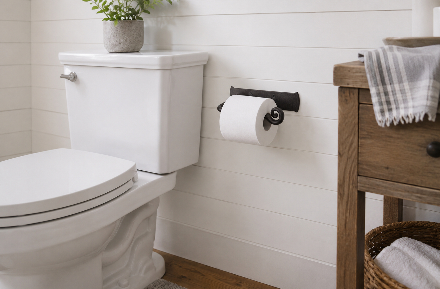 Wall mounted toilet paper holder in black wrought iron installed on white shiplap wall next to toilet and wooden vanity