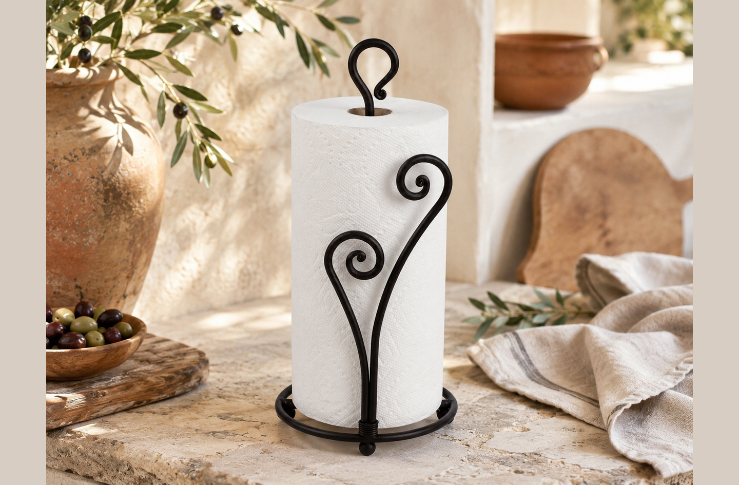 A matte black heart-shaped RTZEN countertop paper towel holder with wrought iron scrollwork stands on a stone countertop beside a wooden bowl of olives.