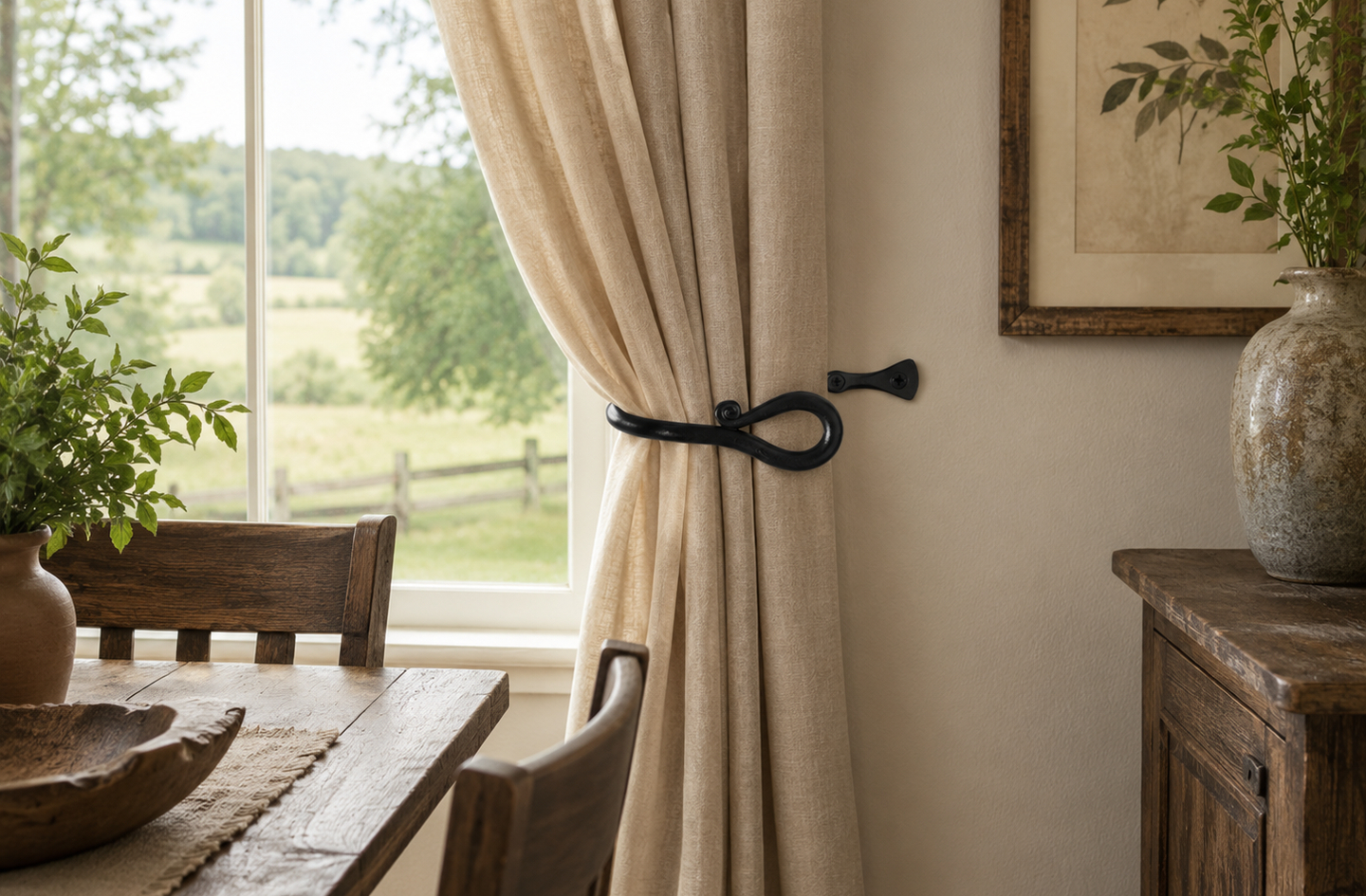 Rustic black metal holdback holding a beige curtain open beside a window overlooking rural fields